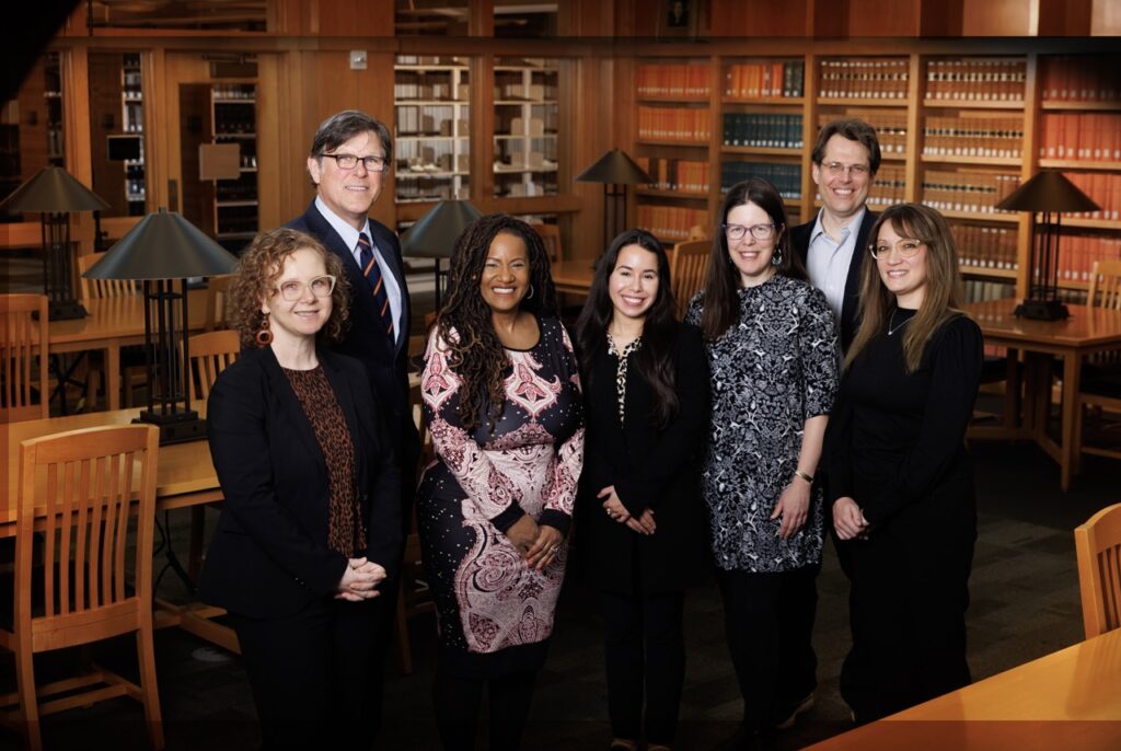Seven individuals stand in library and smile at the camera
