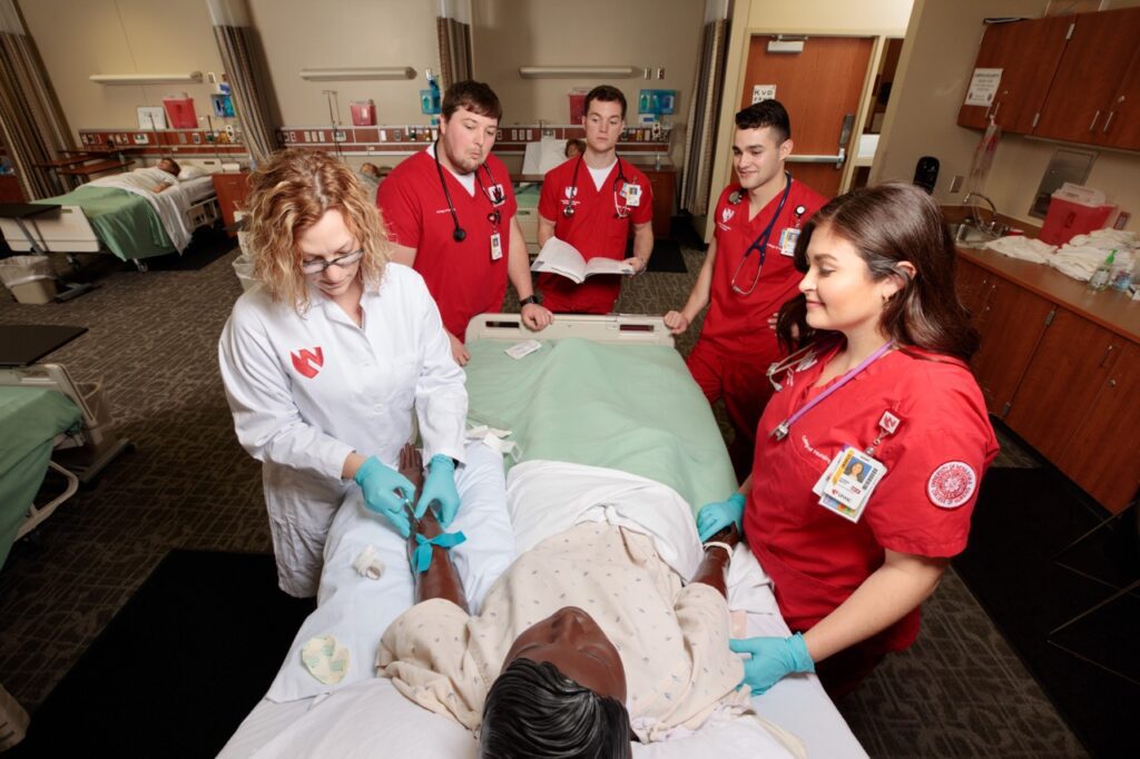 Nursing students surround bed with fake patient alongside their preceptor.