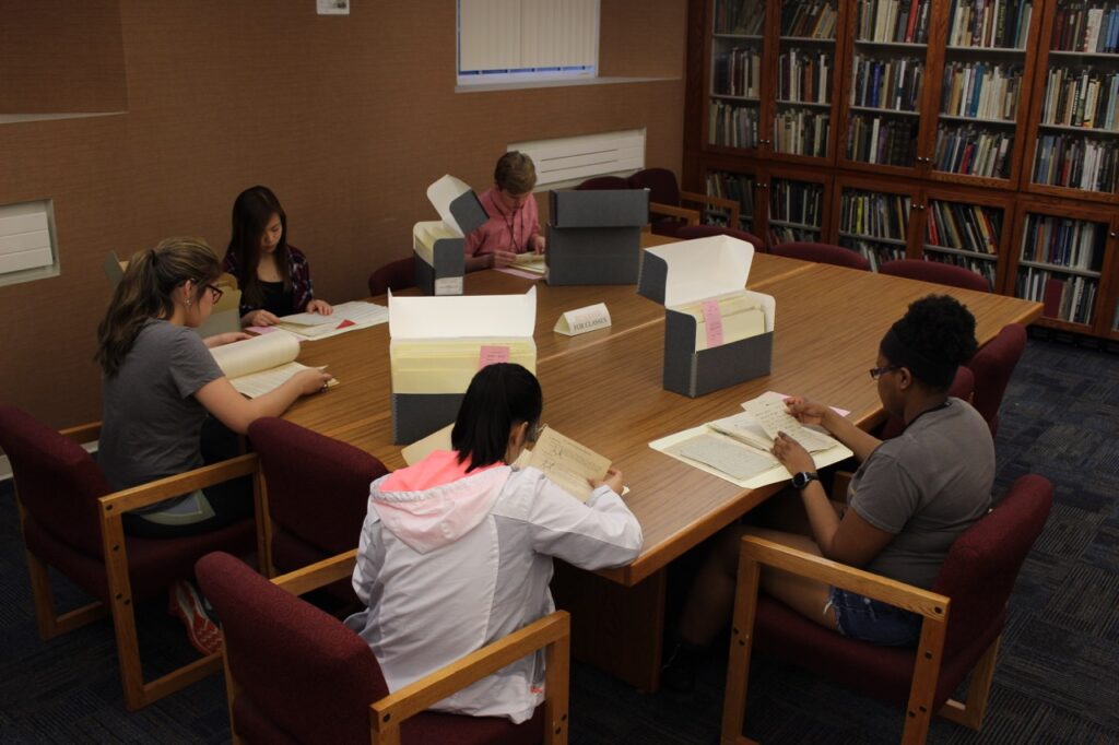 Group of students studying library archives at large table.